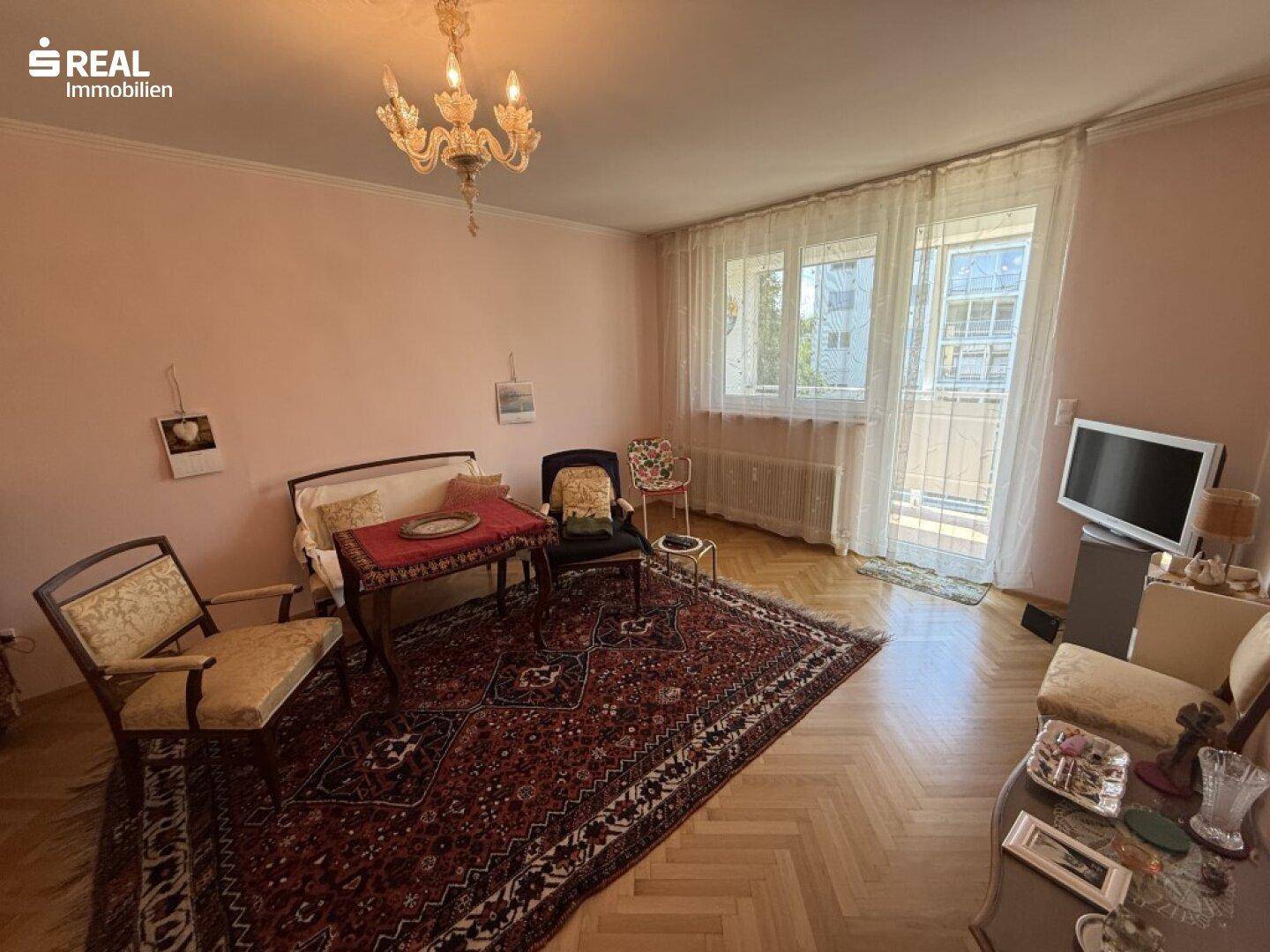 Gemütliches Wohnzimmer mit Fischgrätparkett, traditionellem Teppich und Zugang zum Balkon.