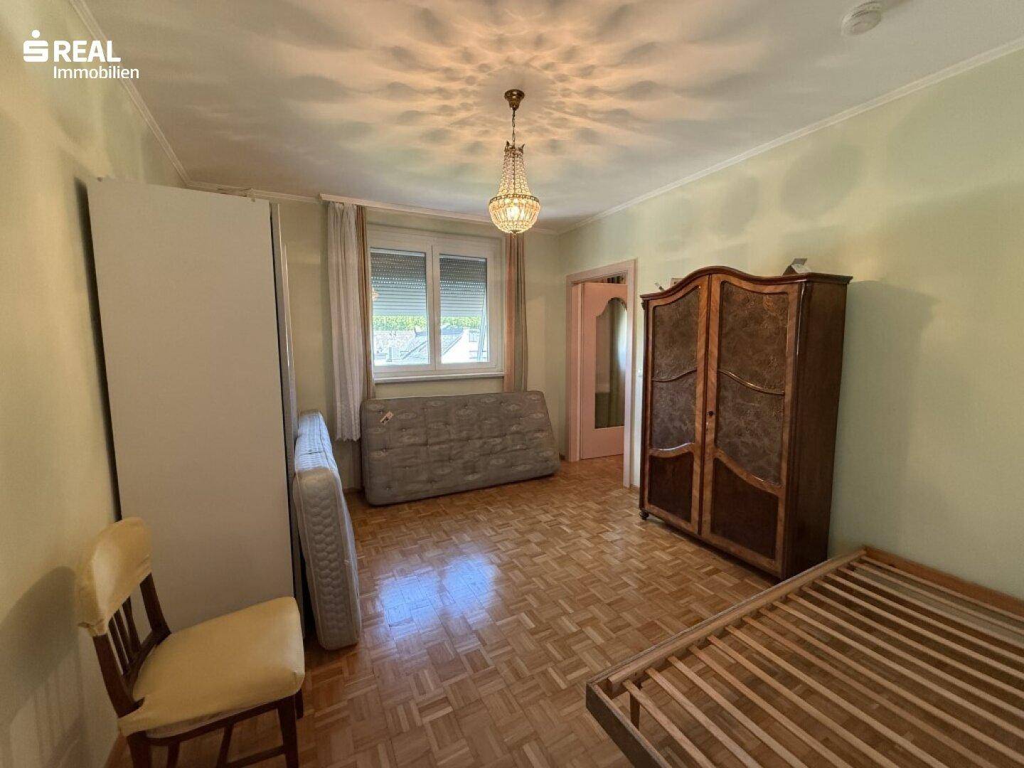 Schlafzimmer mit Parkettboden, großem Kleiderschrank und Fenster mit Rollladen.