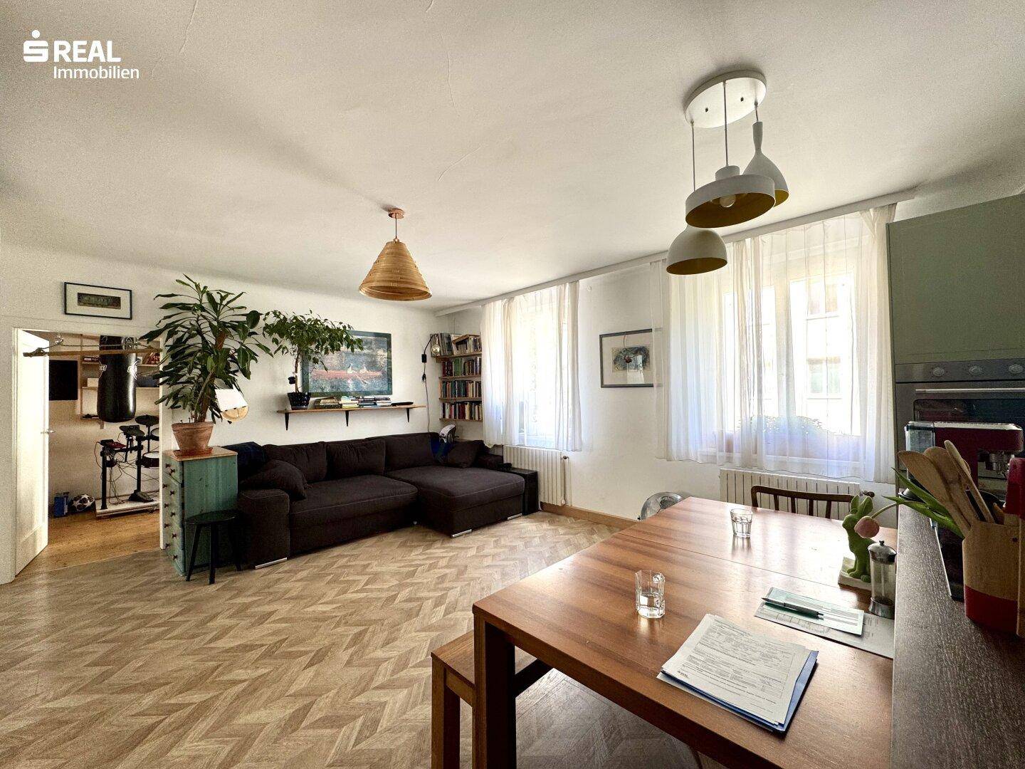 Heller Wohn-Essbereich mit Fischgrätparkett, großem Esstisch und gemütlichem Sofa.