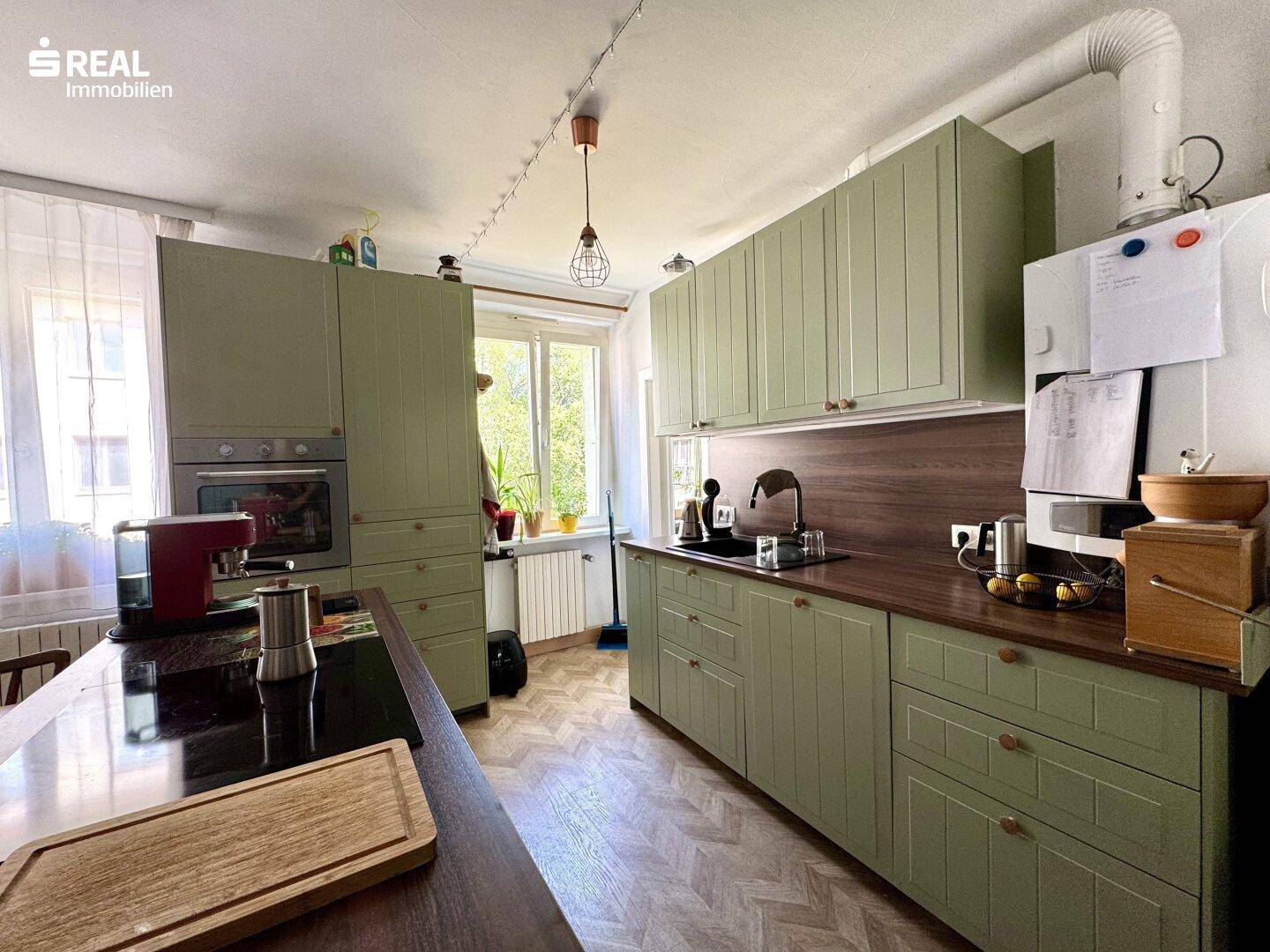 Grüne Einbauküche mit Holz-Arbeitsplatte, integrierten Geräten und Fensterblick ins Grüne.