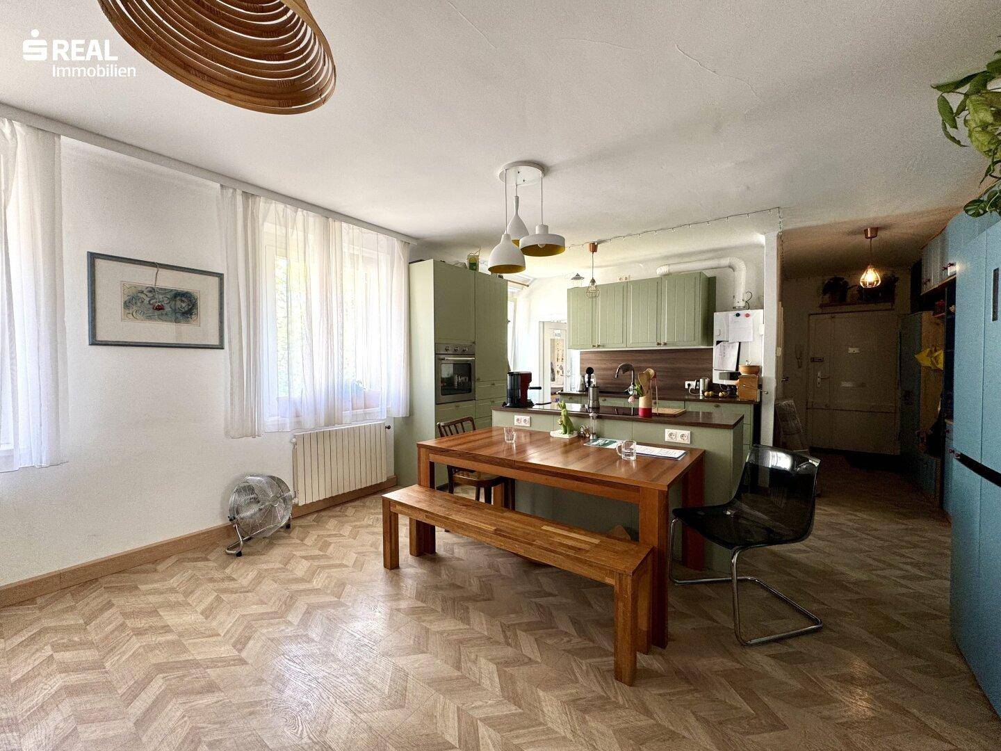 Geräumiger Wohn-Essbereich mit Holztisch, Sitzbank und offener Verbindung zur Küche.
