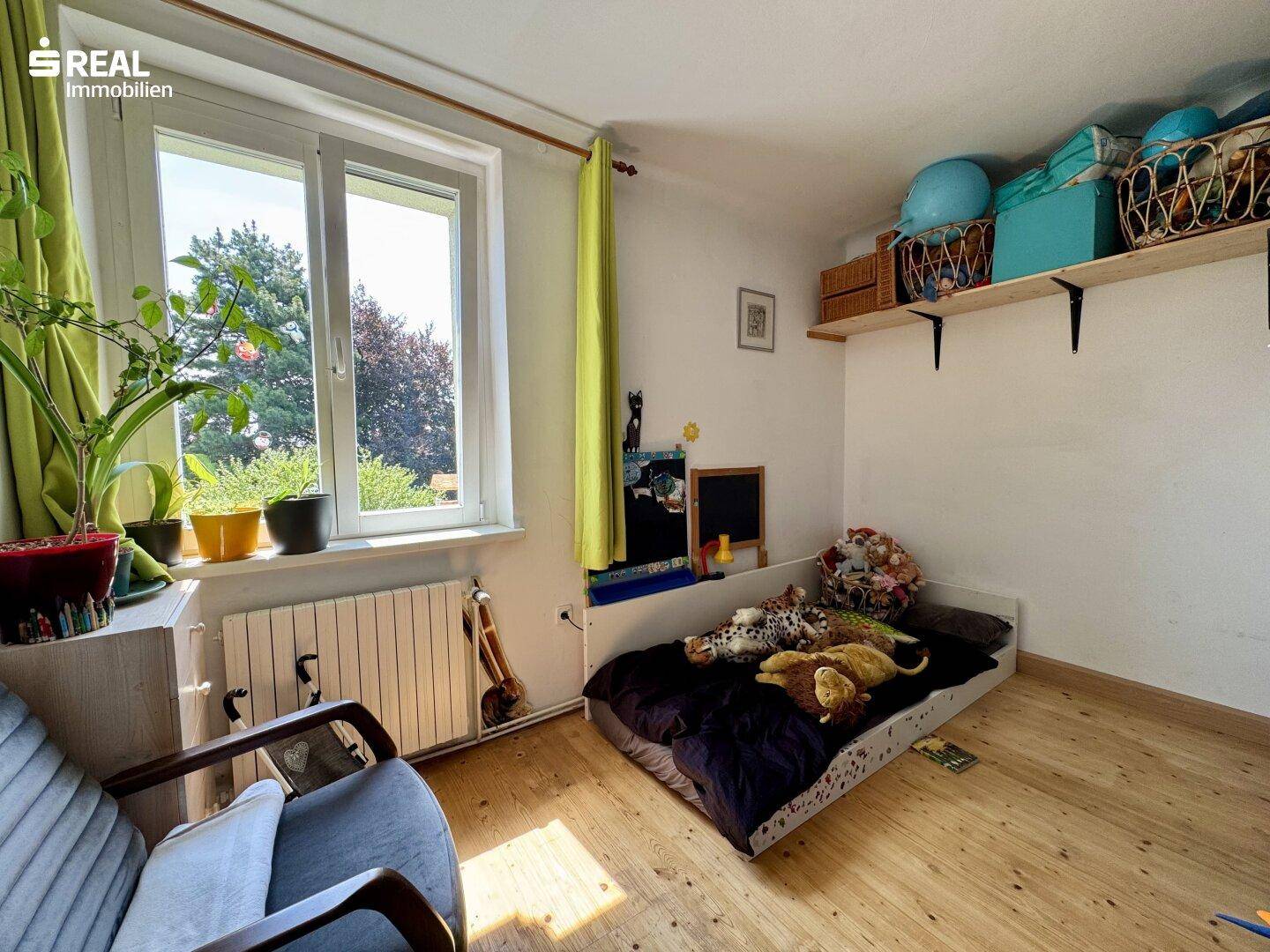 Helles Kinderzimmer mit Holzboden, großem Fenster und Blick ins Grüne.