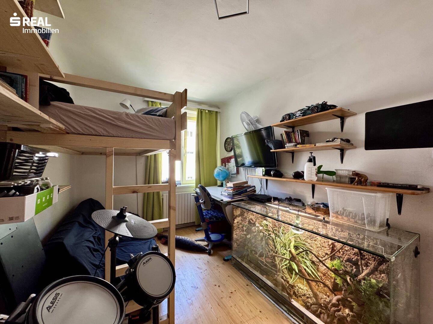 Jugendzimmer mit Hochbett, Schreibtisch, Aquarium und Holzdielenboden.