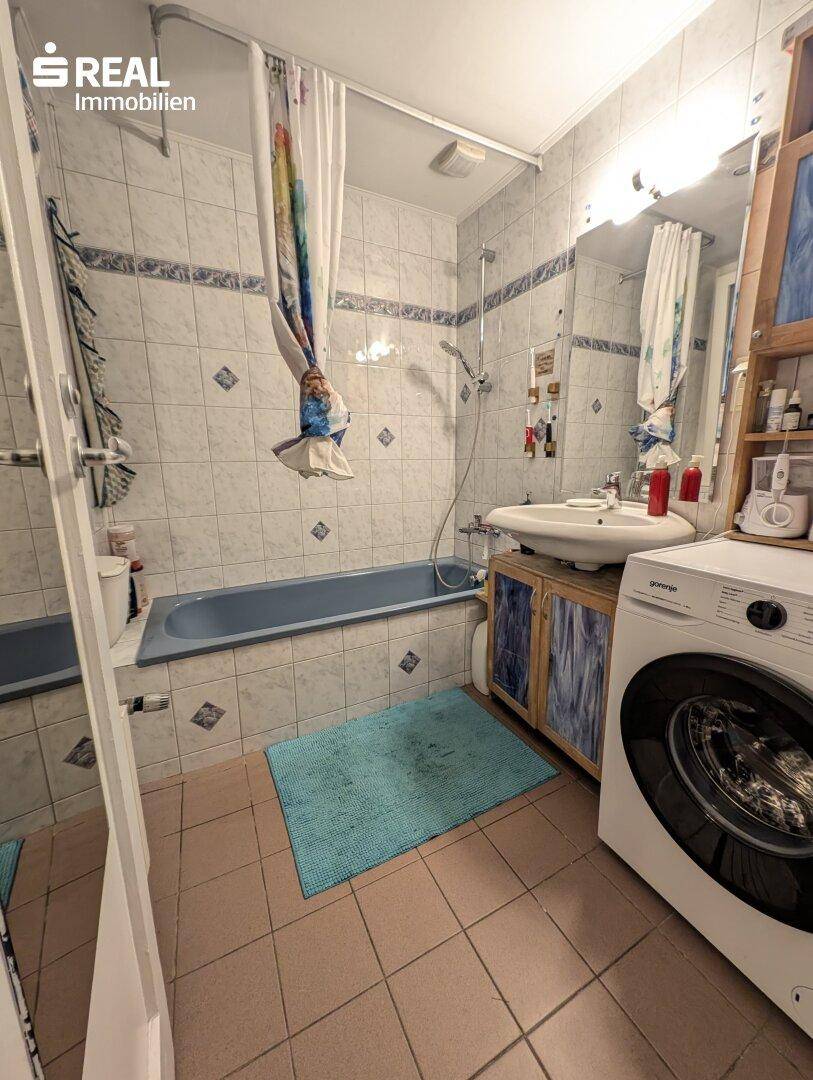 Badezimmer mit Badewanne, Waschbecken, Fliesen und Waschmaschine.