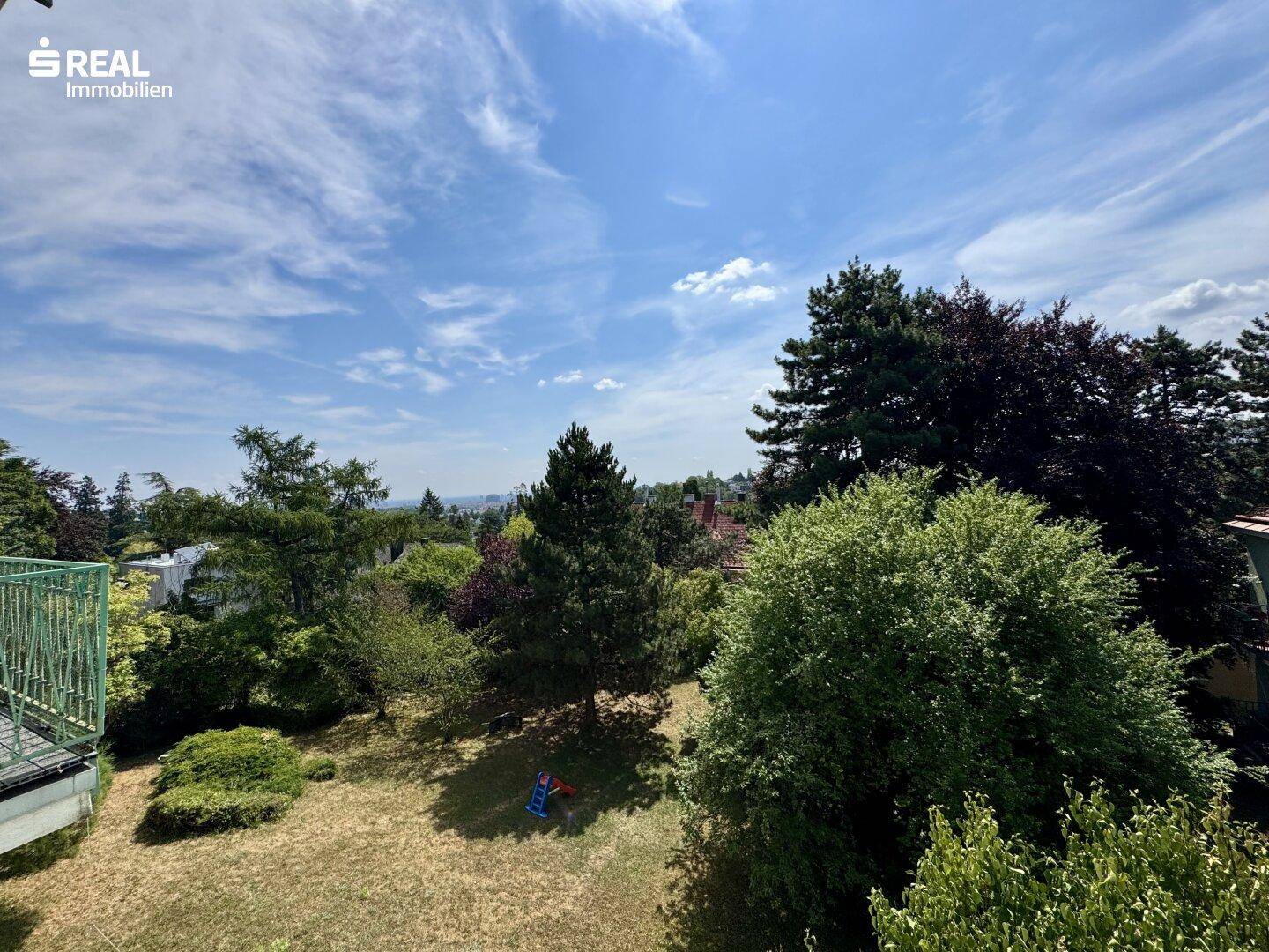 Weitläufiger Gartenbereich mit Rasenfläche, Bäumen und Kinderspielgerät unter blauem Himmel.