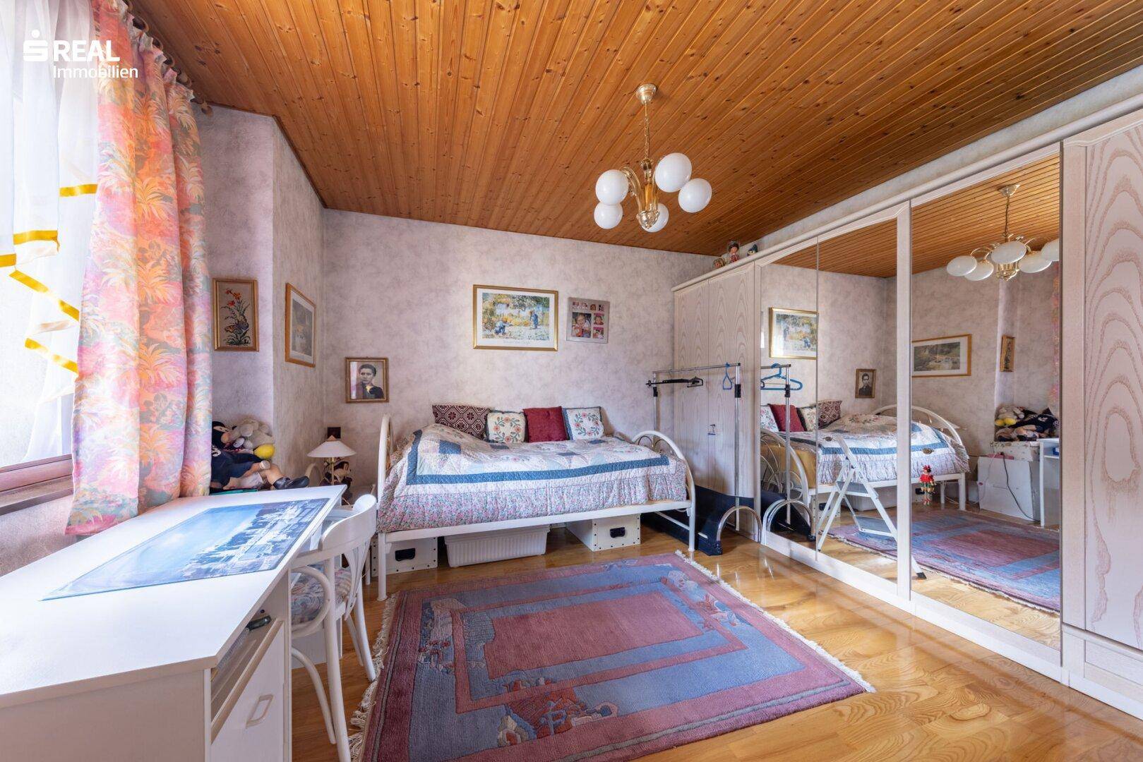Schlafzimmer mit Holzdecke, Spiegelschrank und Schreibtisch.