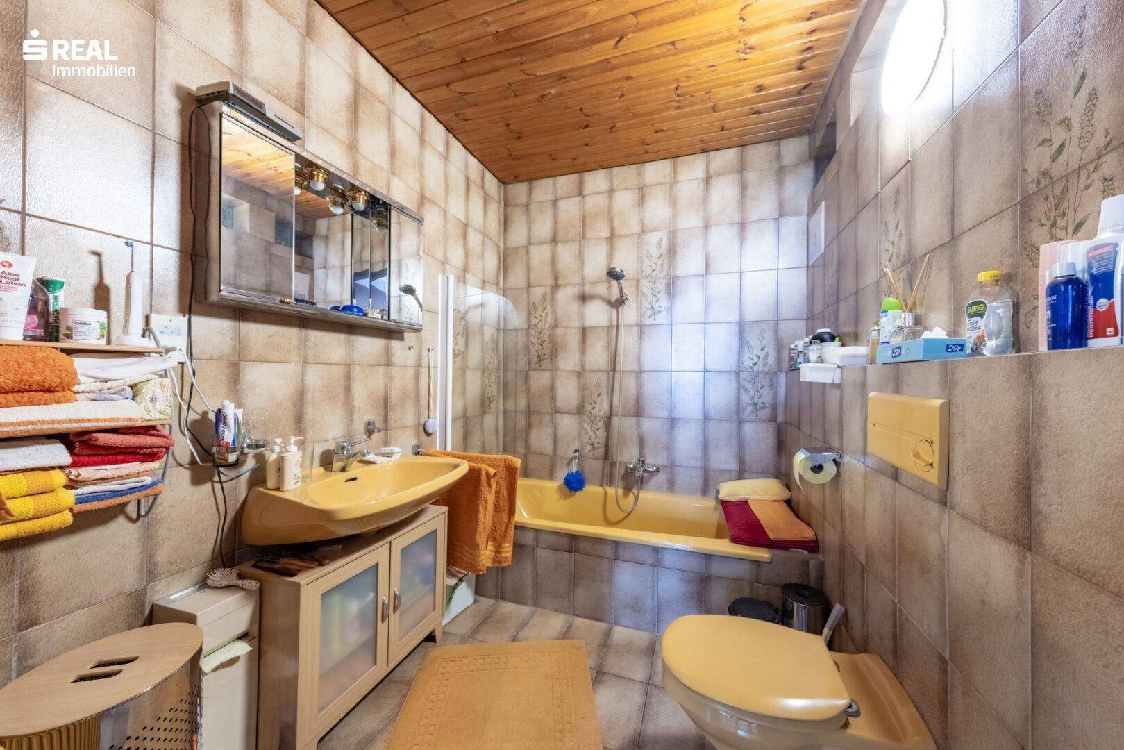 Badezimmer mit gelben Sanitärobjekten, Badewanne und braunen Fliesen.