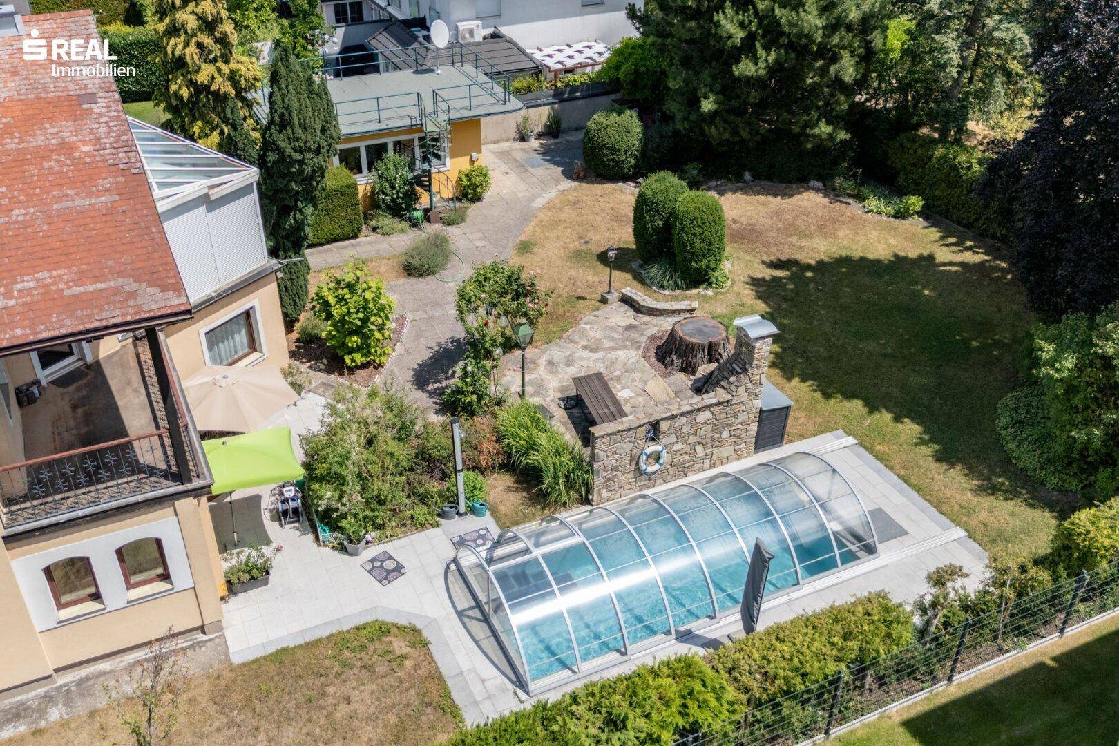 Gartenbereich mit überdachtem Pool, Liegewiese und Blick auf das Haus.