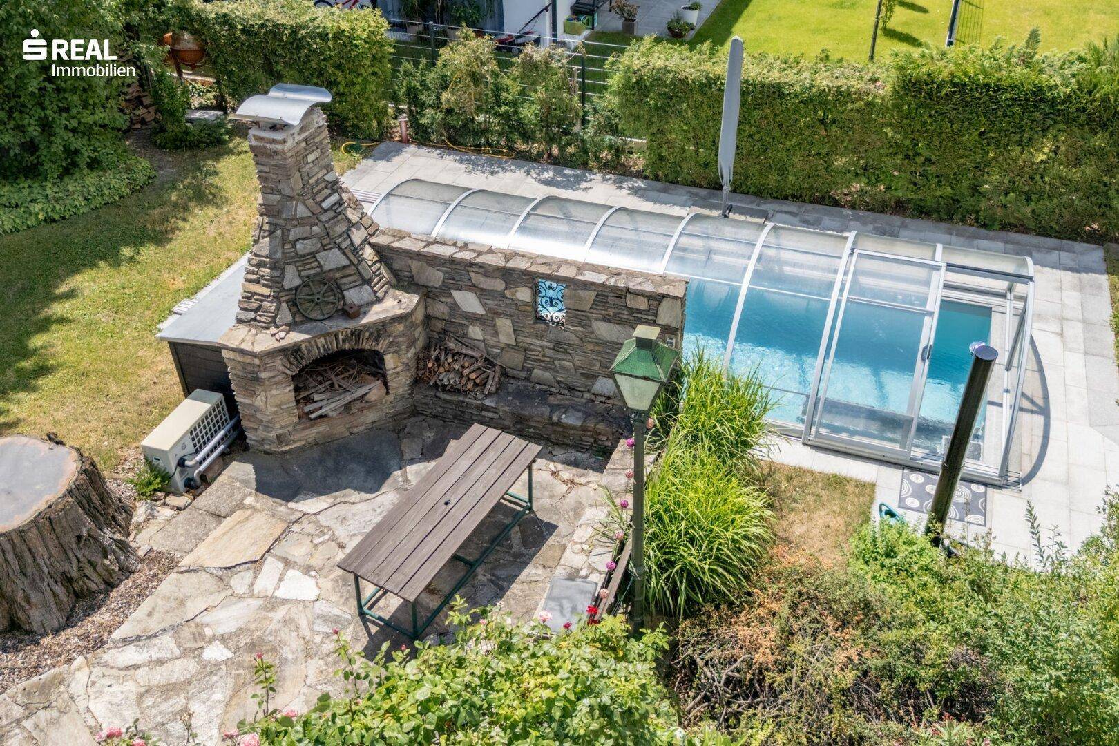 Detailansicht des Grillbereichs mit Steinkamin und des überdachten Pools im Garten.