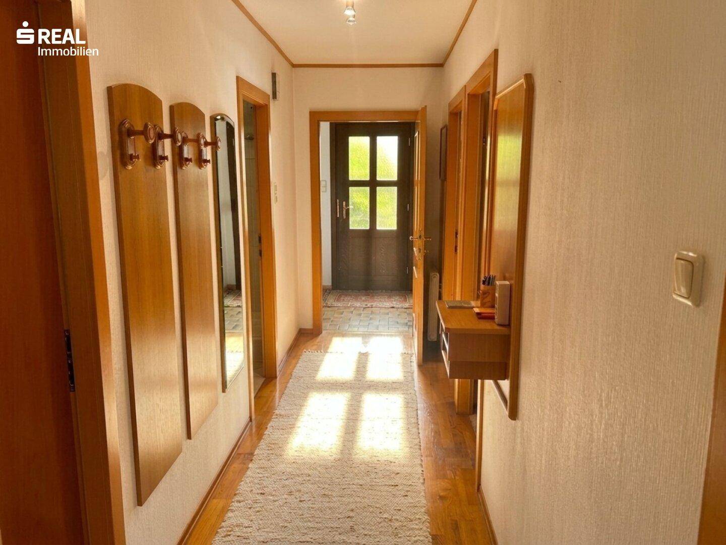Heller Flur mit Holztüren, Garderobe und natürlichem Lichteinfall durch die Eingangstür.