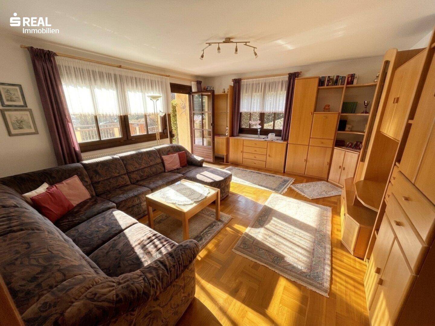 Helles Wohnzimmer mit großem Sofa, Holzschränken und viel natürlichem Licht durch die Fenster.