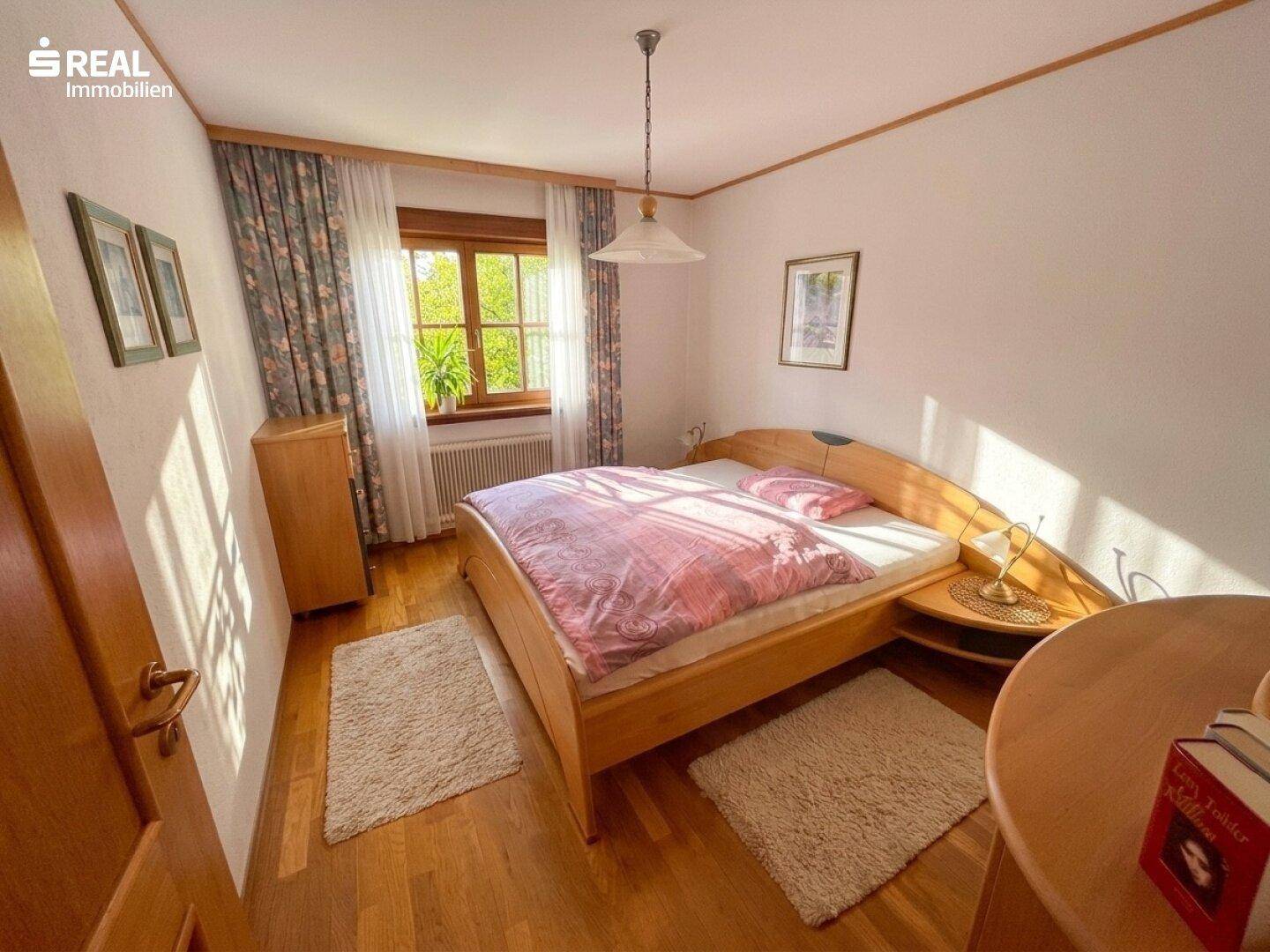 Schlafzimmer mit hellem Holzbett, Nachttischen und einem Fenster mit Blick ins Grüne.