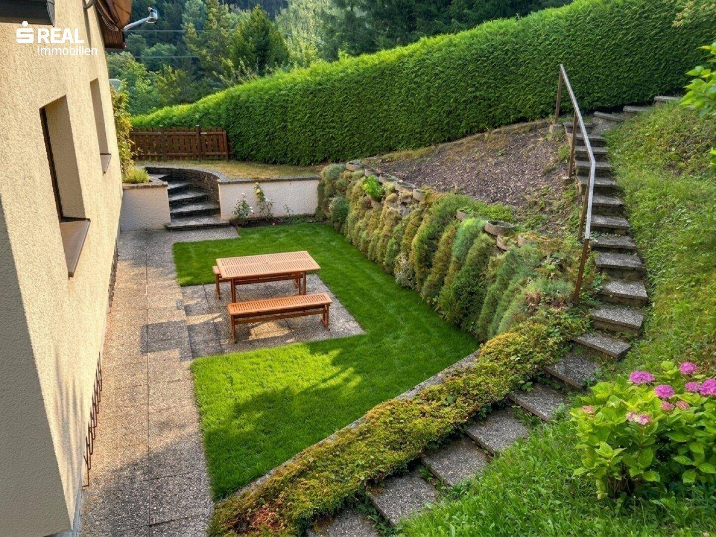 Gestufter Gartenbereich mit Rasenflächen, Steintreppen und einem Picknicktisch.