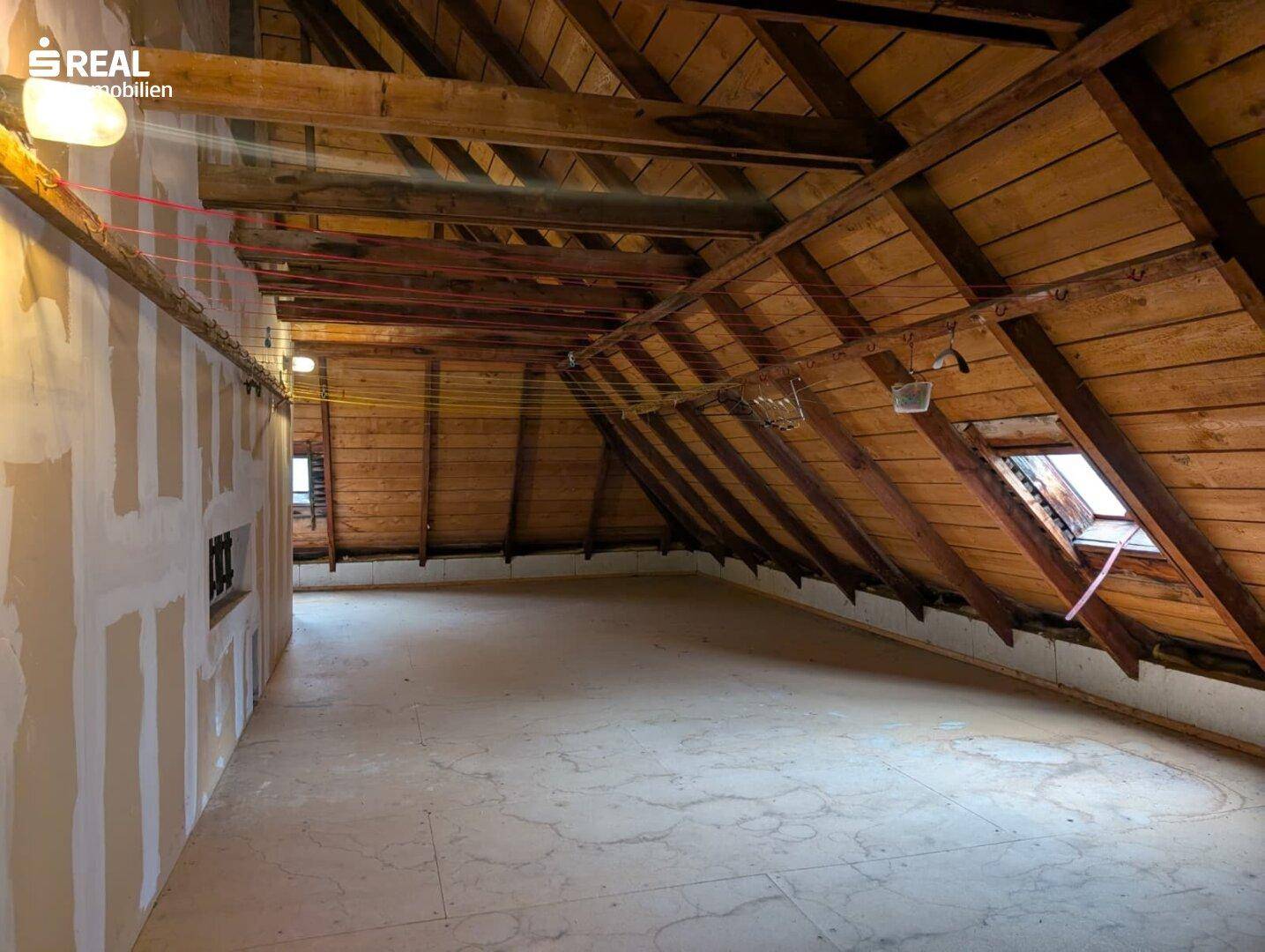 Unfertiger Dachboden mit sichtbaren Holzbalken und Dachfenster, bietet Potenzial für einen Ausbau.