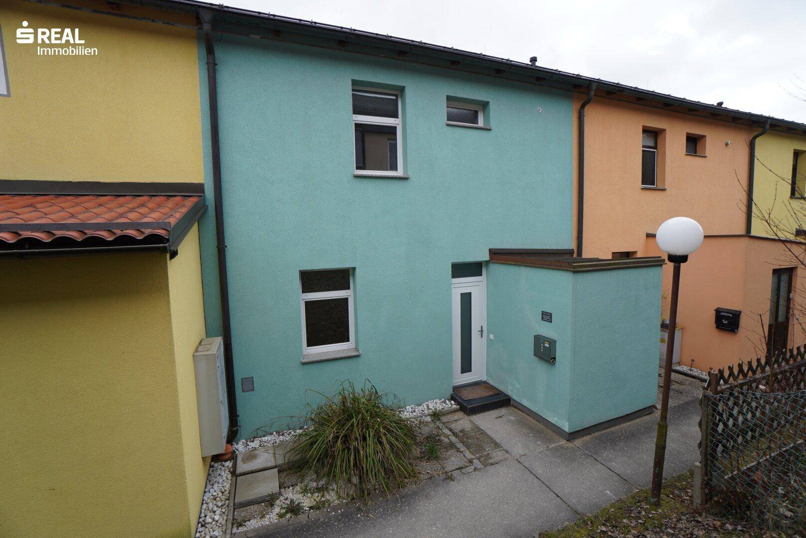 Vorderansicht eines Reihenhauses mit teal-farbener Fassade und Eingangsbereich.