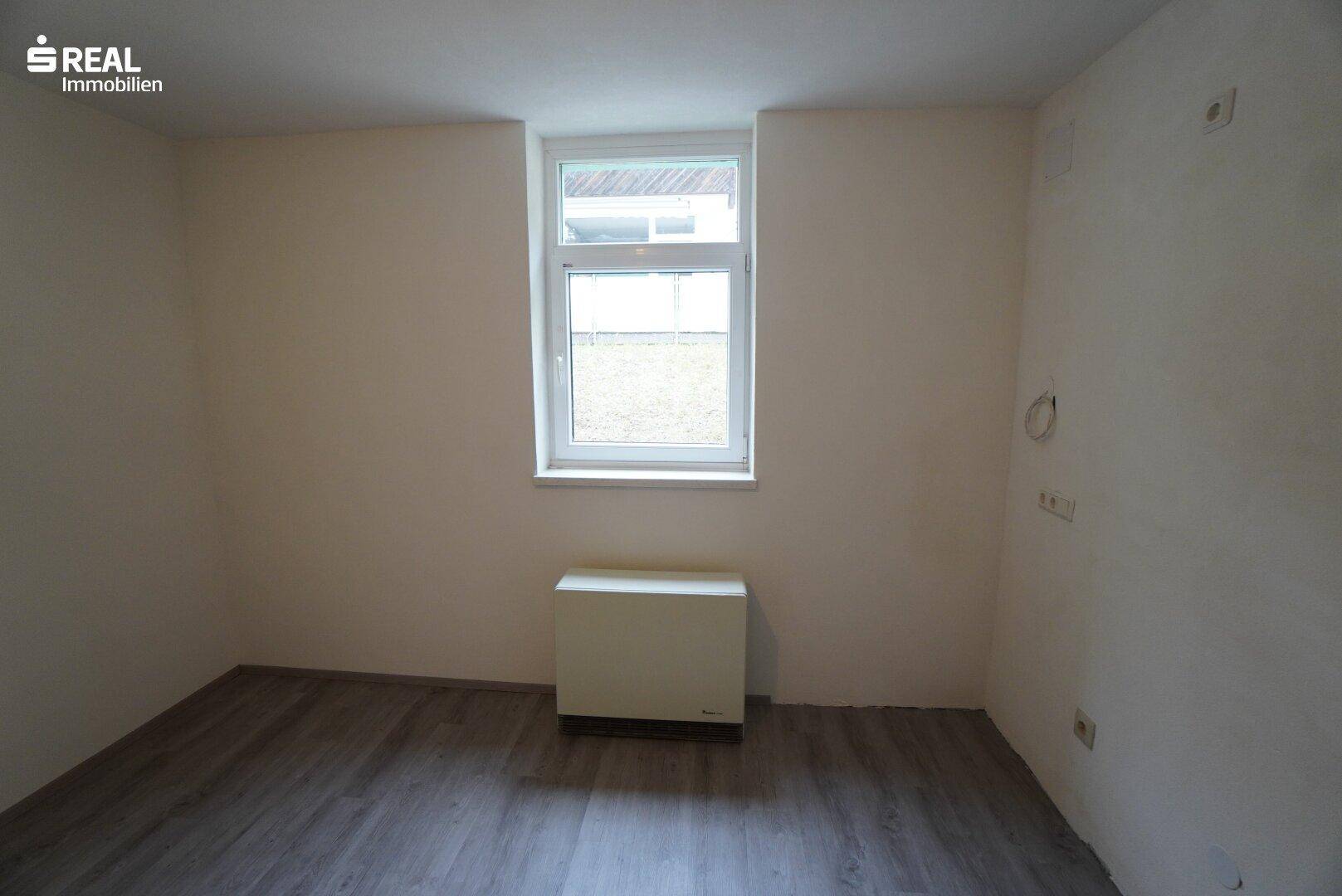 Leerer Raum mit Fenster und Laminatboden, bereit zur individuellen Gestaltung.