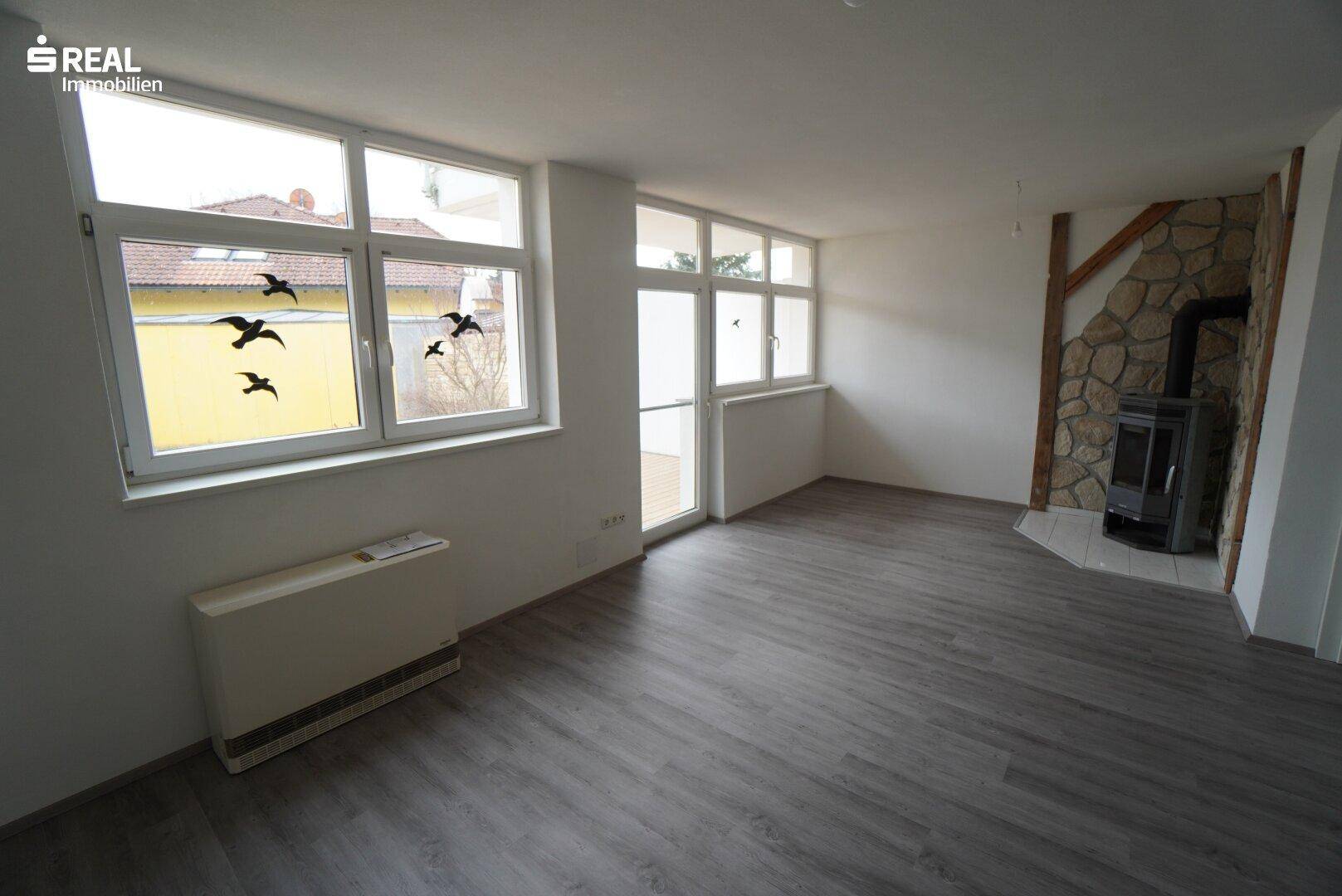 Geräumiges Wohnzimmer mit Kaminofen, Laminatboden und großen Fenstern.