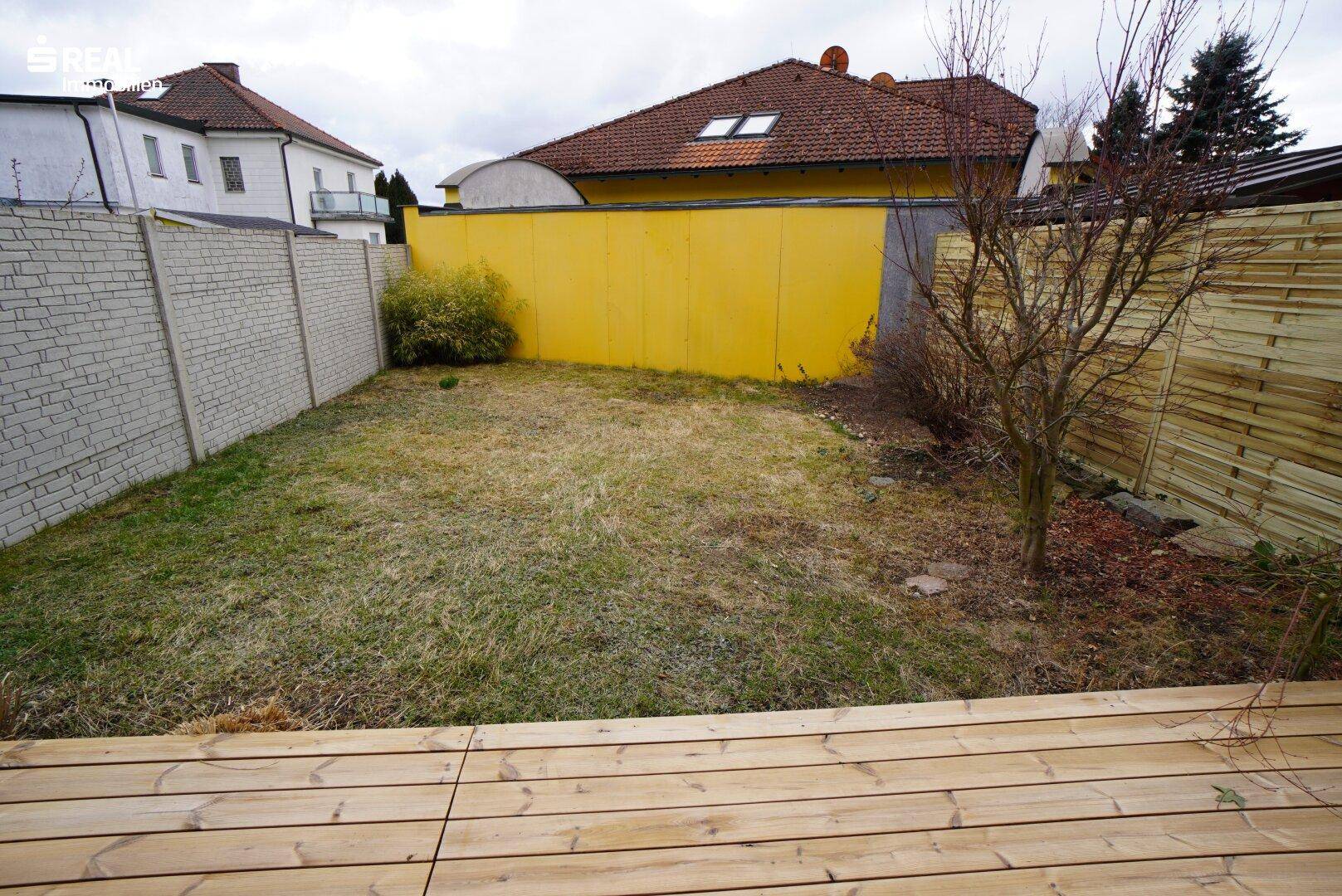 Gartenbereich mit Holzterrasse und Rasenfläche, ideal für Entspannung im Freien.