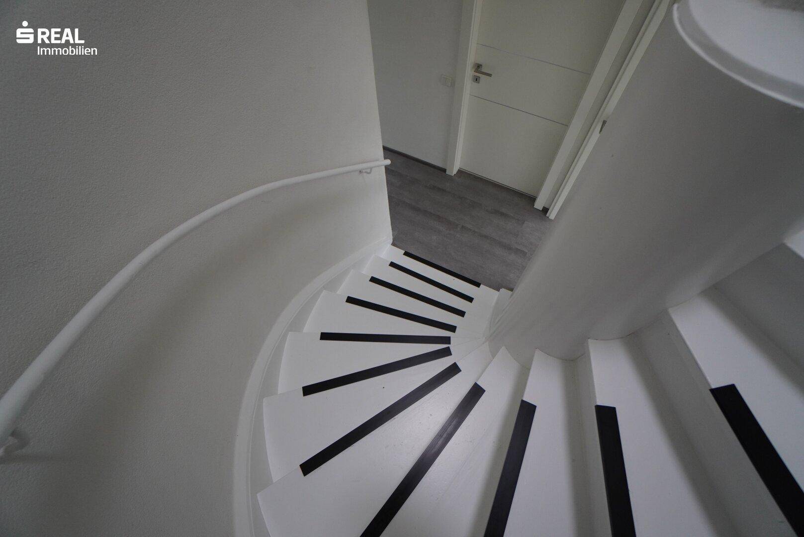 Wendeltreppe mit weißem Geländer und dunklen Akzenten, die die Etagen verbindet.