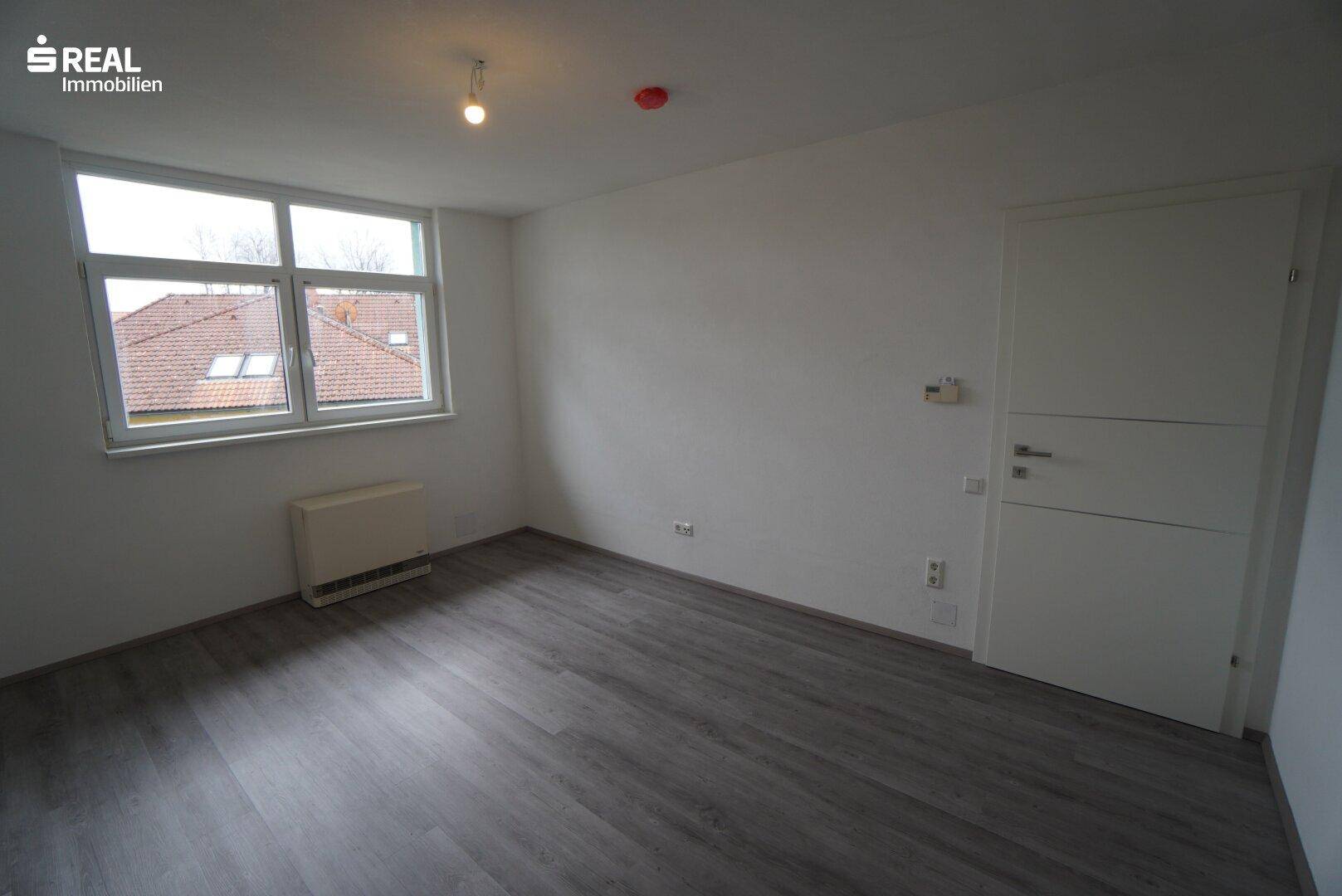 Geräumiges Schlafzimmer mit Laminatboden und Blick ins Grüne.