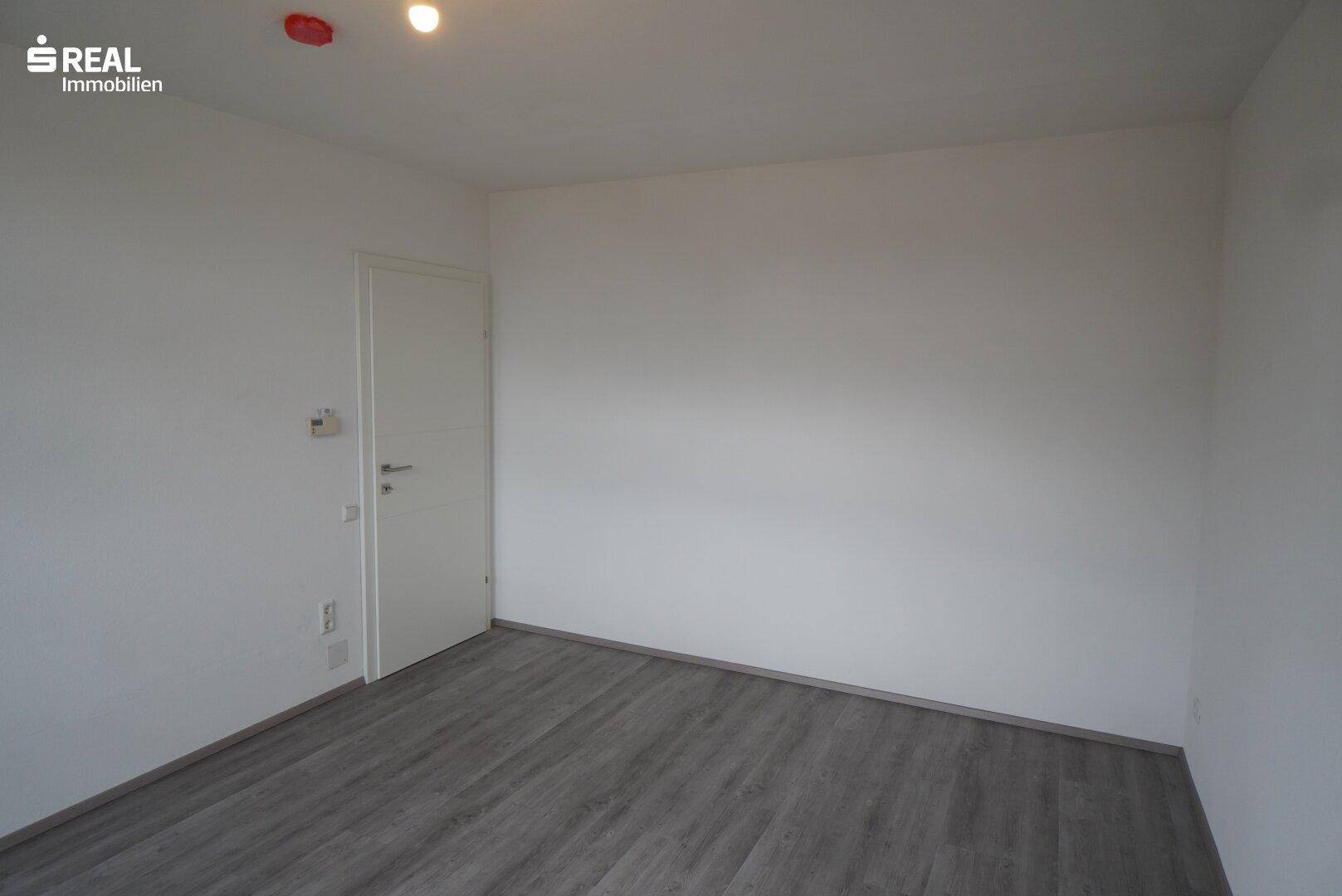 Helles Schlafzimmer mit Laminatboden und weiß gestrichenen Wänden.