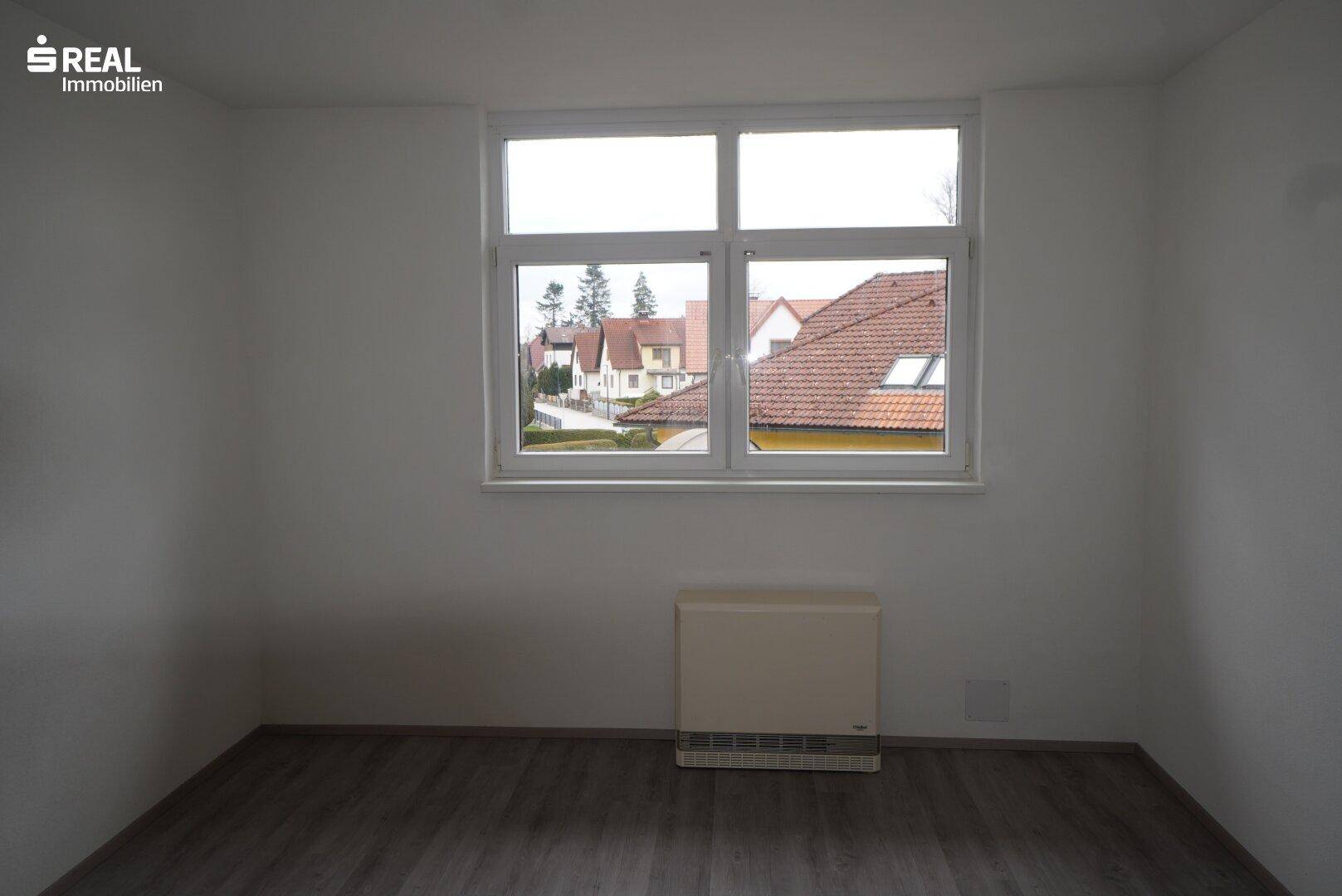 Heller Raum mit Fensterblick auf die Nachbarschaft und einem Heizkörper an der Wand.