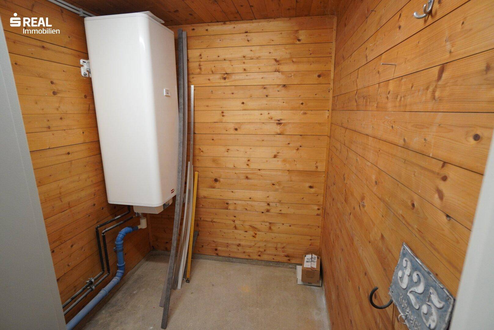 Praktischer Hauswirtschaftsraum mit Holzverkleidung, Warmwasserbereiter und sichtbaren Leitungen.