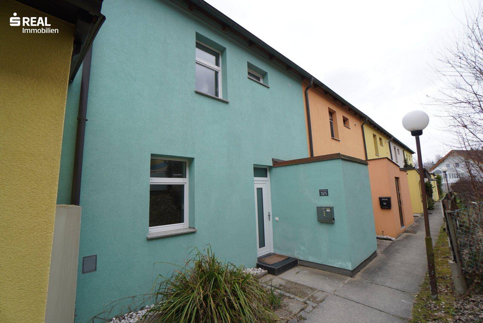 Vorderansicht eines Reihenhauses mit auffälliger türkiser Fassade und Eingangsbereich.