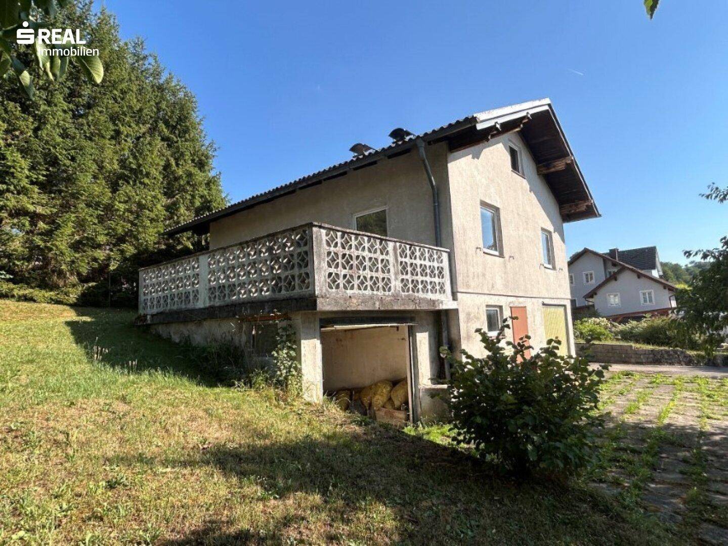 Seitenansicht des Hauses mit Betonbalkon und Zugang zu einem offenen Untergeschossbereich.