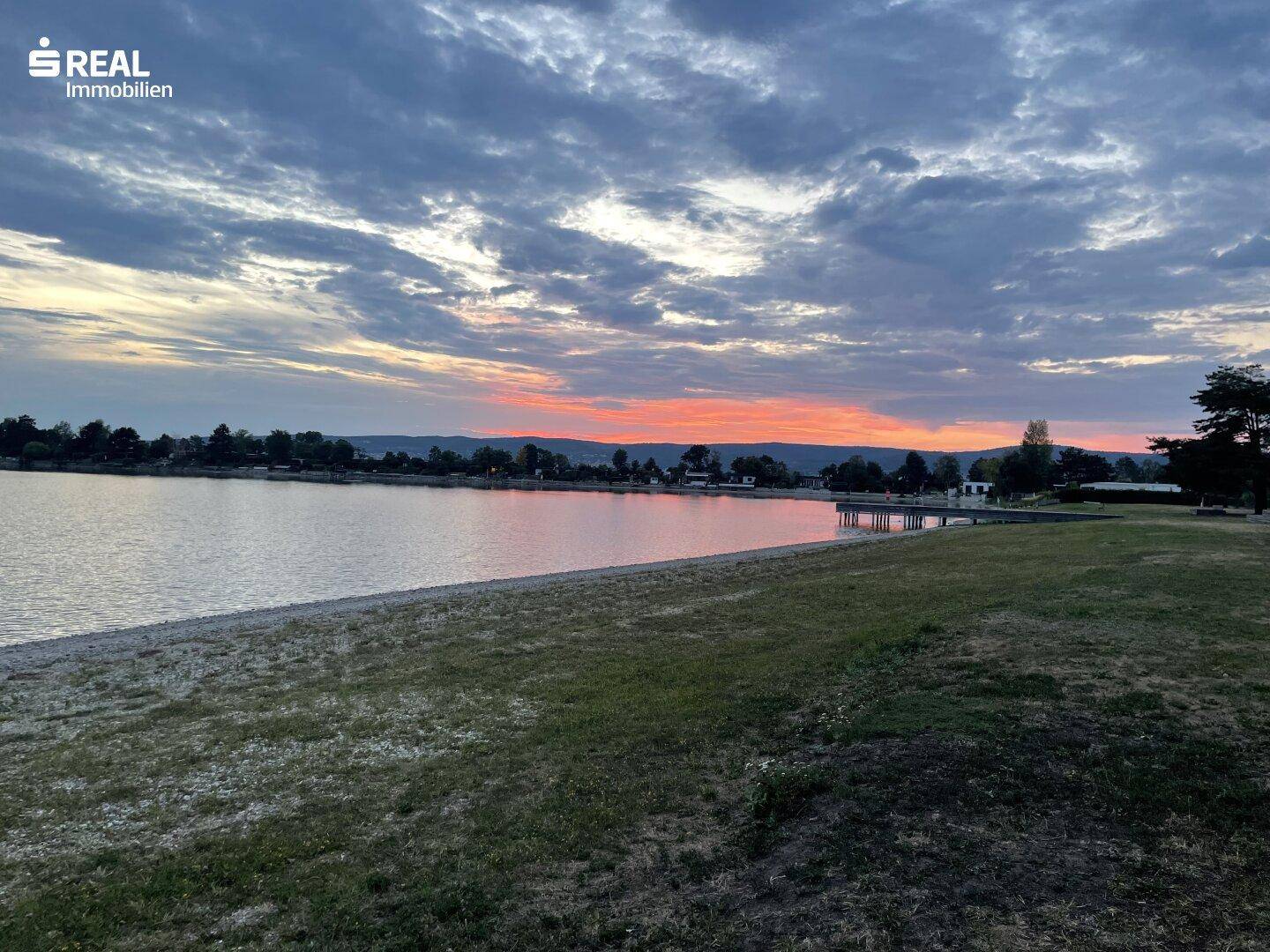 Malerischer Sonnenuntergang über dem See mit einem schmalen Strand und einer Bergkette am Horizont.