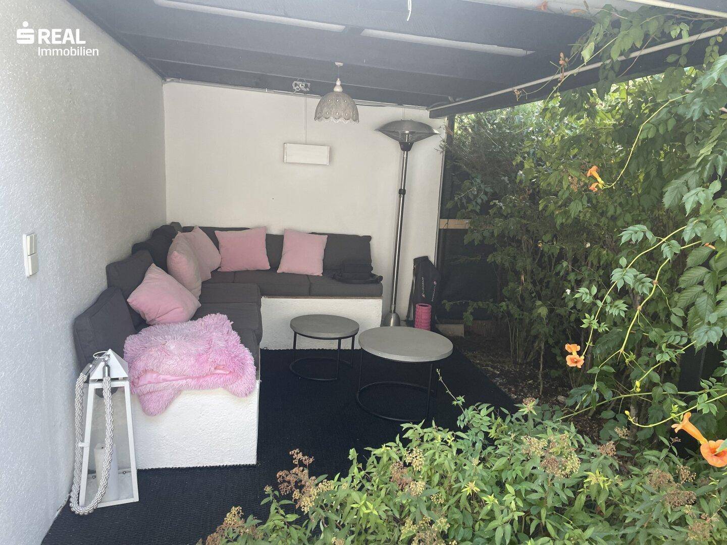 Gemütlicher überdachter Sitzbereich im Freien mit Ecksofa, Kissen und Pflanzen für entspannte Stunden.
