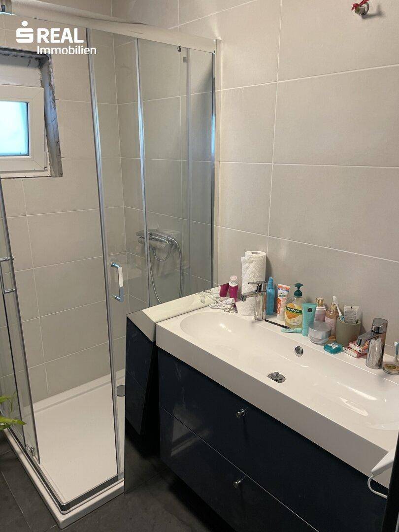 Modernes Badezimmer mit begehbarer Dusche, Einzelwaschbecken und grauen Fliesen, hell und funktional.