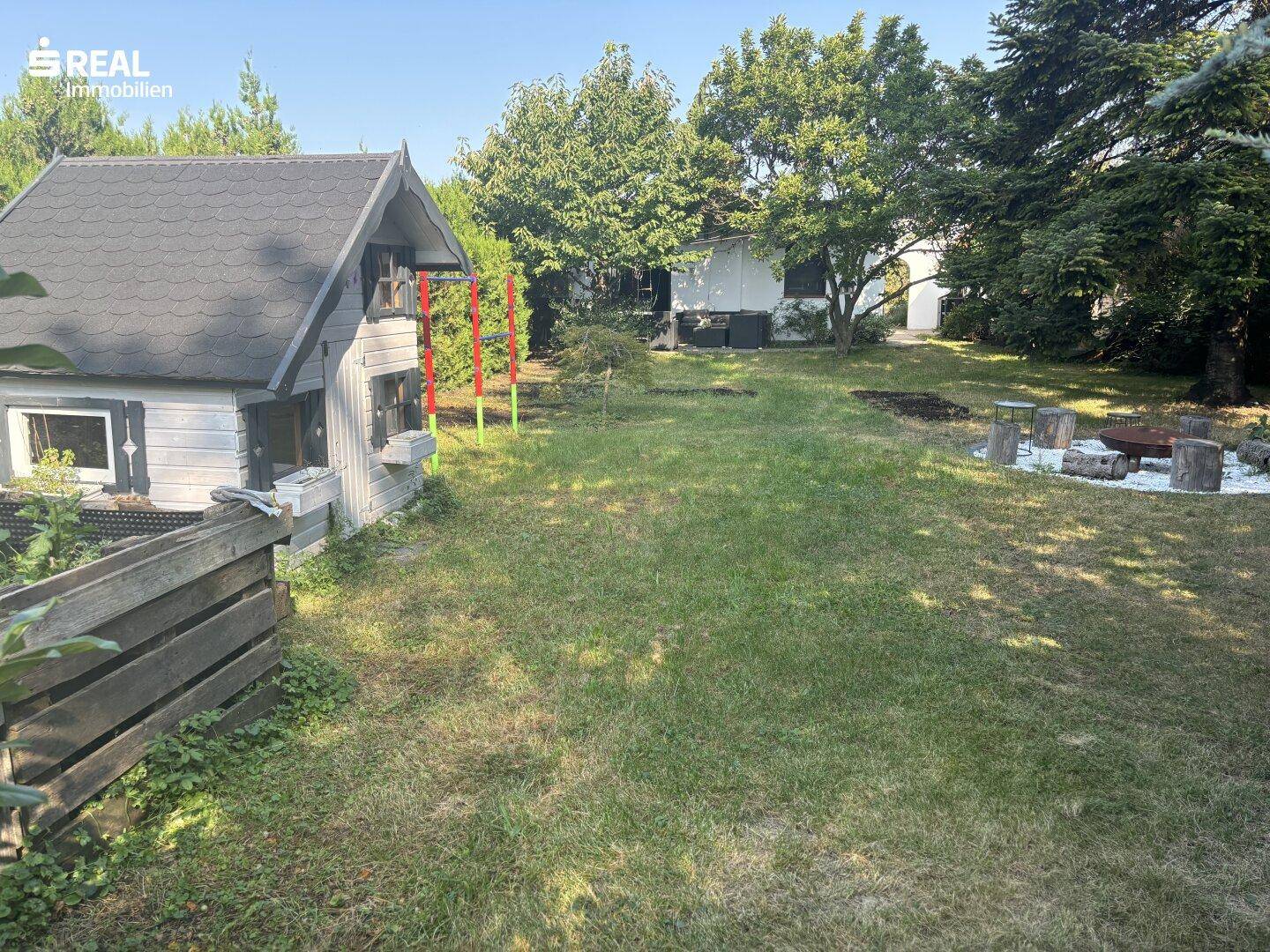 Weitläufiger Garten mit Spielhaus, Feuerstelle und gepflegtem Rasen, ideal für Familienaktivitäten.