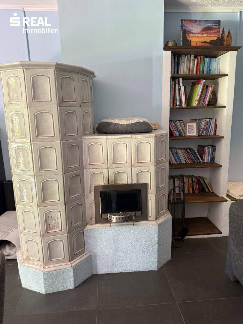 Detailansicht eines traditionellen Kachelofens mit Feuerstelle, daneben ein integriertes Bücherregal.