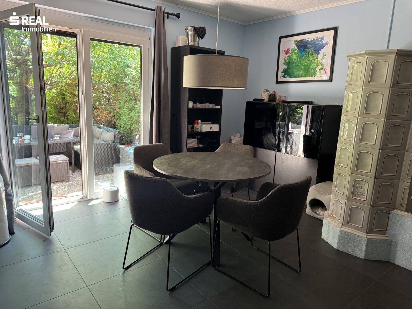 Essbereich mit rundem Tisch und Stühlen, neben einem Kachelofen und Terrassenzugang für Mahlzeiten im Freien.