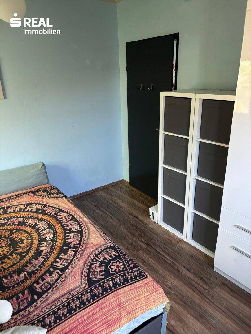 Ecke eines Zimmers mit Tagesbett, weißem Regal und einer dunklen Tür, alles in hellblauen Wänden.