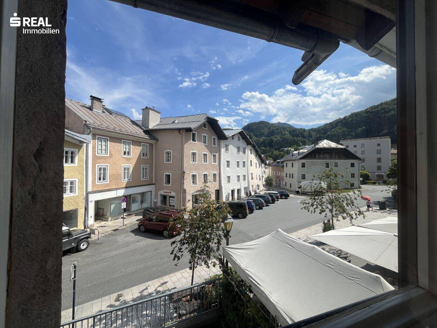 Blick aus dem Fenster auf eine belebte Straße mit historischen Gebäuden und Bergen im Hintergrund.