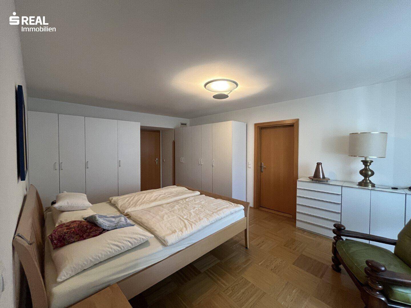 Helles Schlafzimmer mit Doppelbett, weißen Einbauschränken und klassischem Parkettboden.