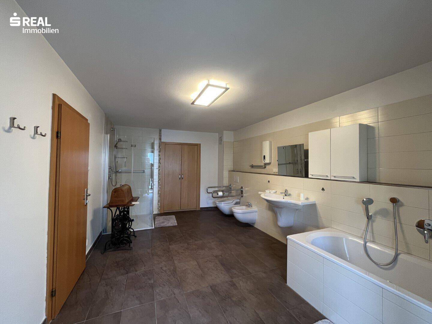 Geräumiges Badezimmer mit Badewanne, Dusche, Doppelwaschbecken und dunklen Fliesen.
