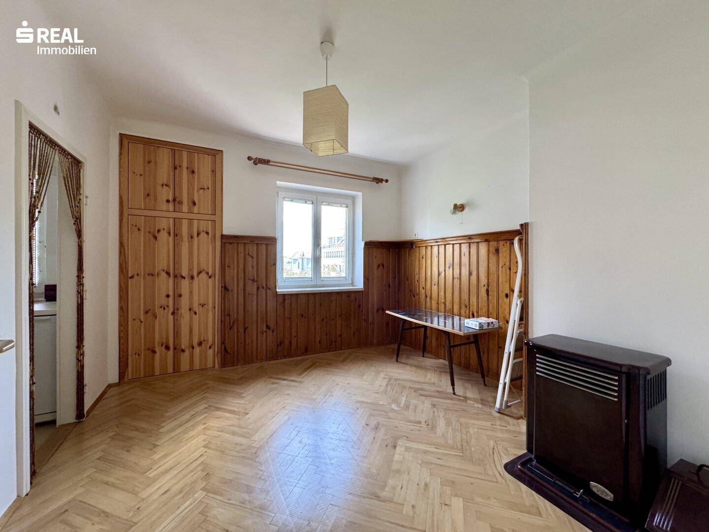 Geräumiges Zimmer mit Fischgrätparkett, Holzvertäfelung und einem Ofen, bereit zur Einrichtung.