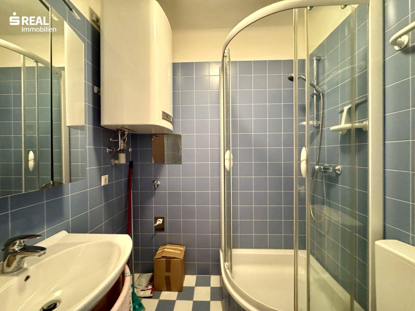 Badezimmer mit blauen Fliesen, Duschkabine und Waschbecken, ausgestattet mit einem Boiler.