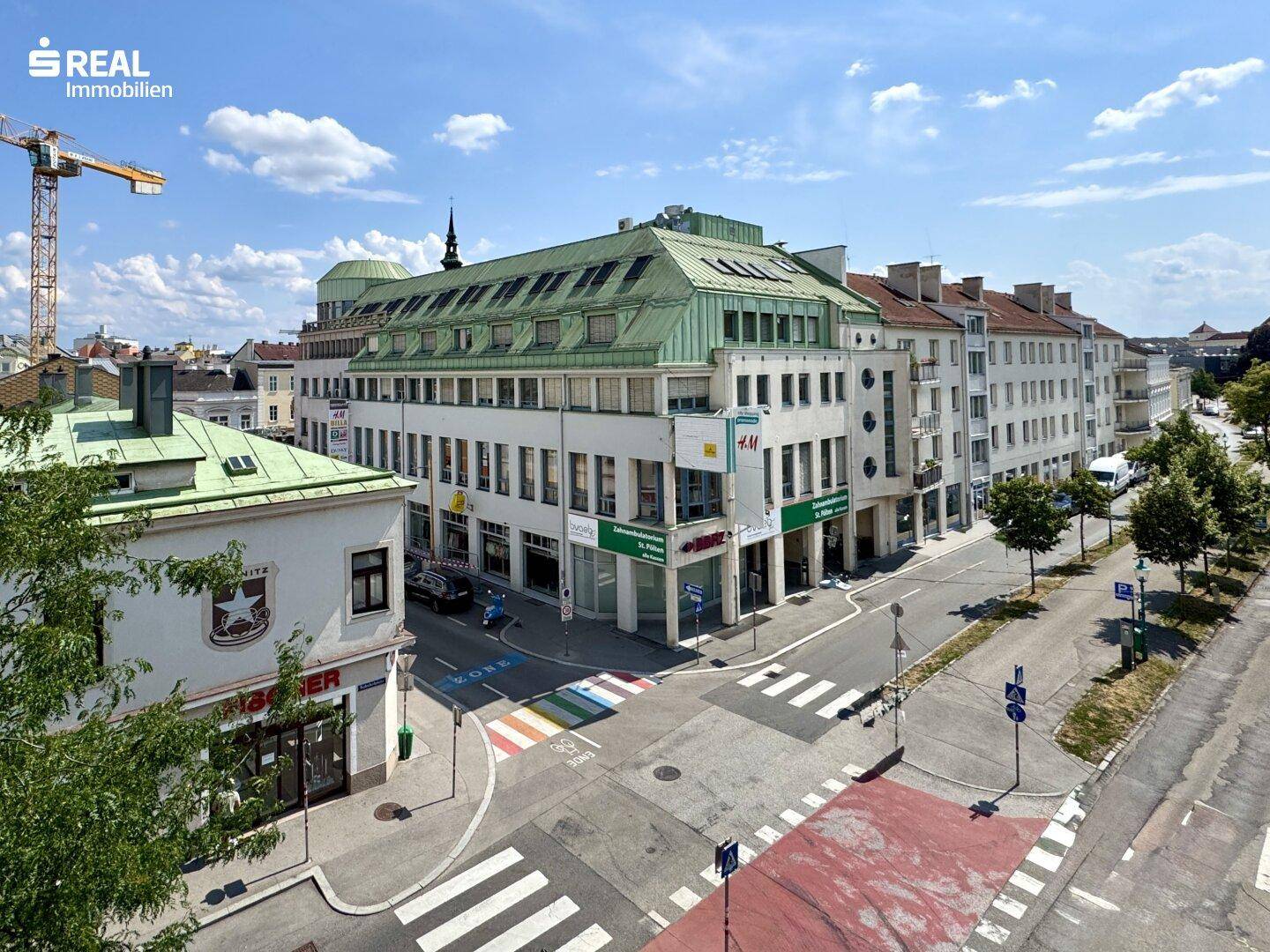 Weitläufiger Blick auf eine belebte Stadtkreuzung mit Geschäften und Gebäuden unter blauem Himmel.