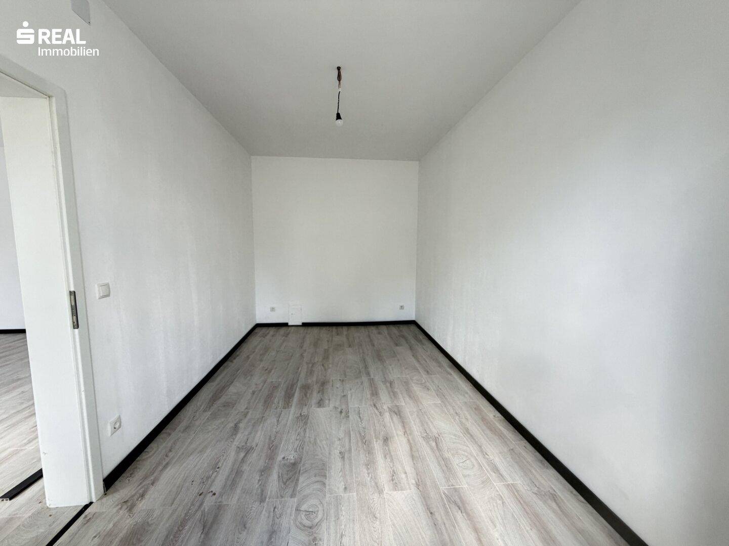 Langes, helles Zimmer mit neuem Laminatboden und frisch gestrichenen weißen Wänden.
