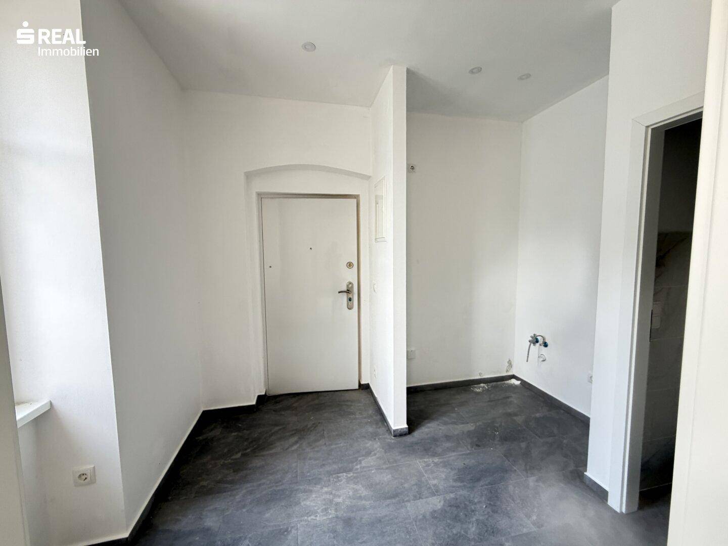 Eingangsbereich mit Sicherheitstür, dunklen Fliesen und weißen Wänden, mit Anschlussmöglichkeiten.