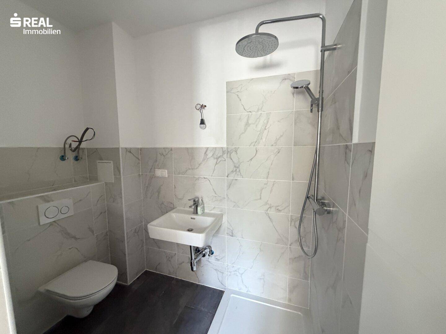 Modernes Badezimmer mit Regendusche, Hänge-WC und eleganten Marmorfliesen an den Wänden.