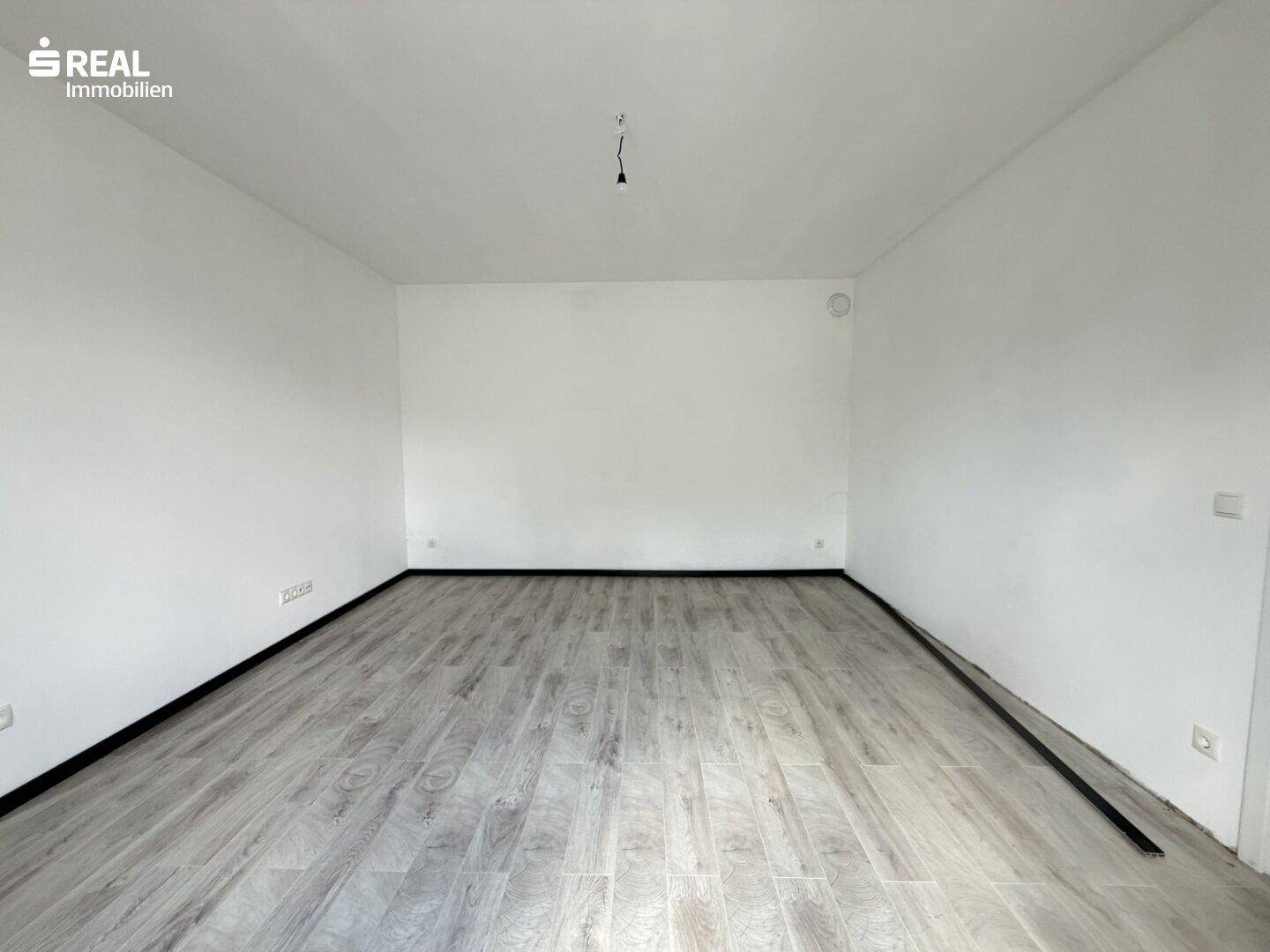 Geräumiges, helles Zimmer mit neu verlegtem Laminatboden und sauber gestrichenen Wänden.