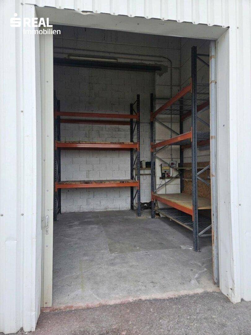 Blick in den Lagerraum durch eine große offene Tür, mit industriellen Regalen und Betonboden.