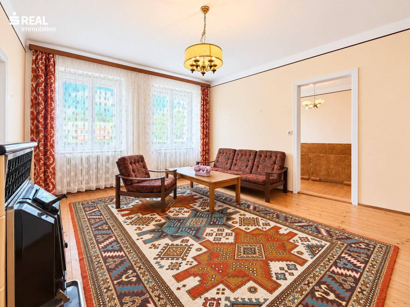 Gemütliches Wohnzimmer mit traditionellem Teppich, Holzfußboden und einem Ofen als Heizquelle.