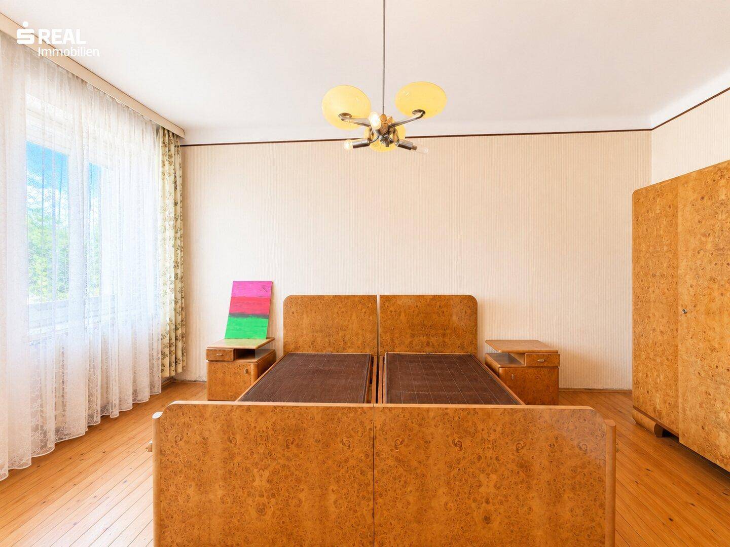 Schlafzimmer mit zwei Einzelbetten, Holzfußboden und großem Fenster für viel Tageslicht.