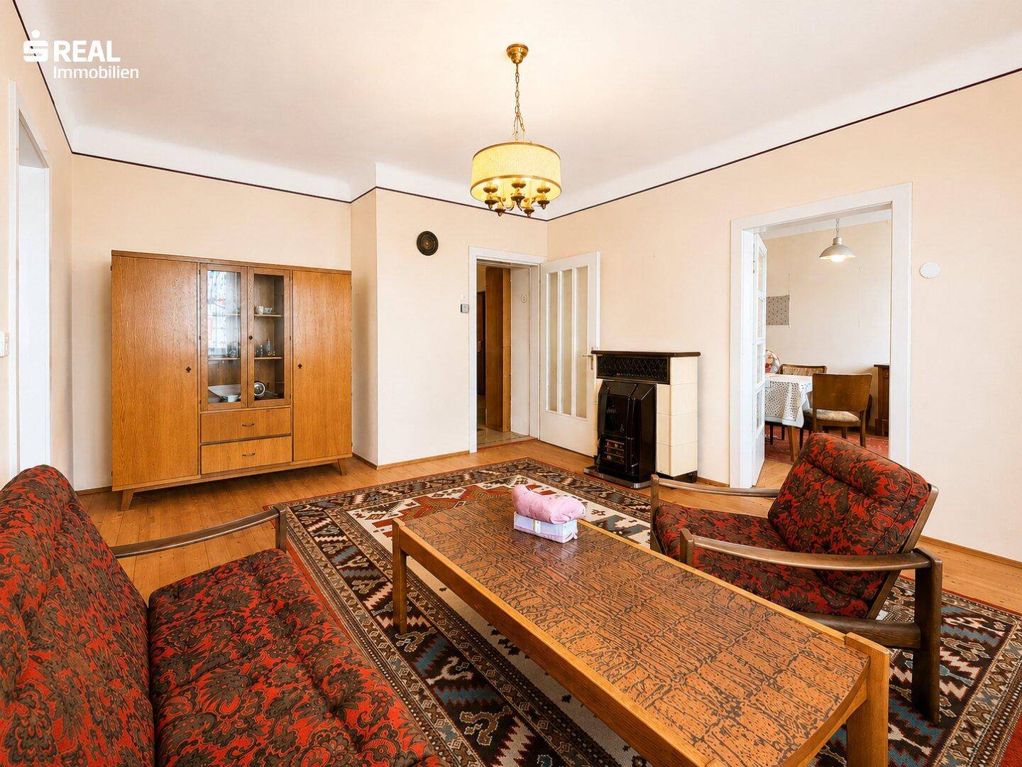 Wohnzimmer mit traditionellen Möbeln, Teppich und einem Holzofen als Heizquelle.